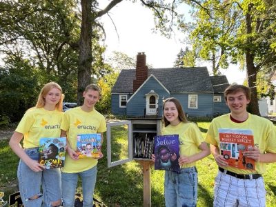 Enactus Carthage students flank a Little Free Library, which is a component of their DiversiReads project